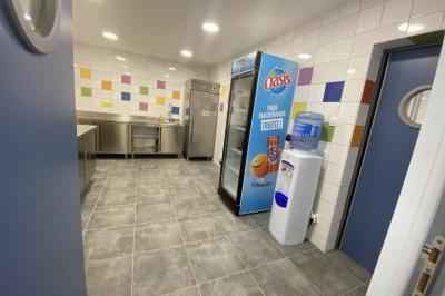 Miniature Cuisine Entrée d'un parking clôturé devant des bâtiments industriels avec des panneaux publicitaires sur la clôture.