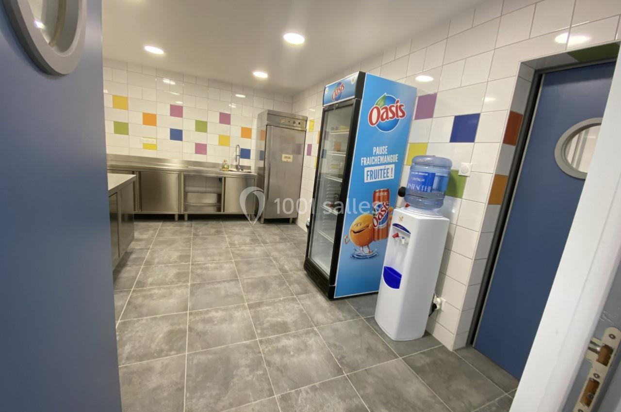 Cuisine équipée avec carrelage mural coloré, réfrigérateur, distributeur d'eau et plans de travail en inox.