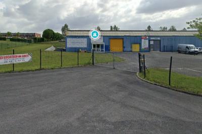 Miniature Exterieur Entrée d'un parking clôturé devant des bâtiments industriels avec des panneaux publicitaires sur la clôture.