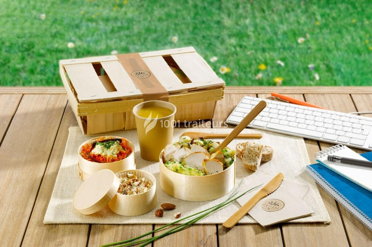 Repas sain présenté dans des contenants en bois sur une table en extérieur, avec clavier et carnet à proximité.