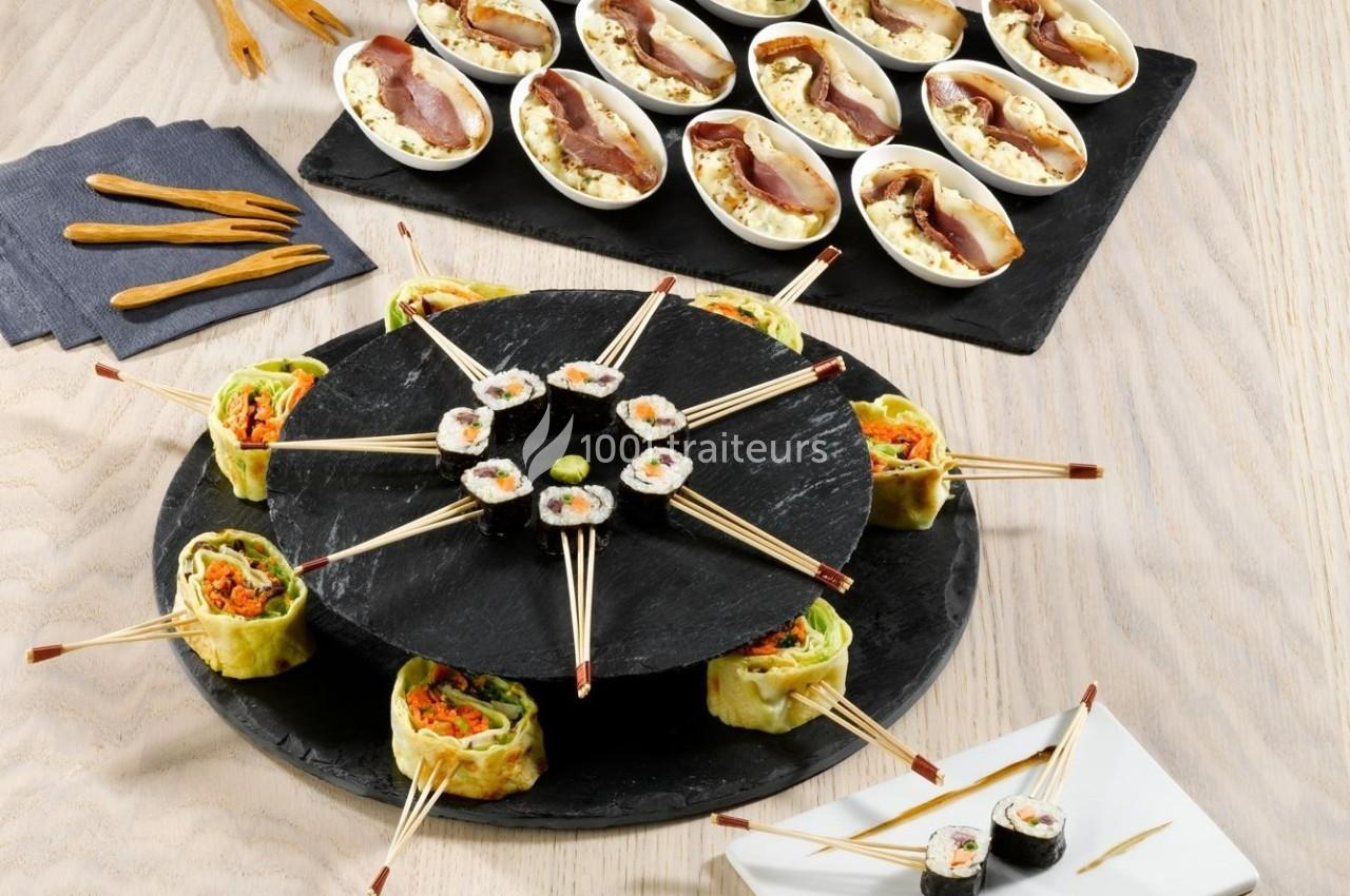 Assortiment de sushis et bouchées apéritives disposés sur des plateaux en ardoise et une assiette blanche.