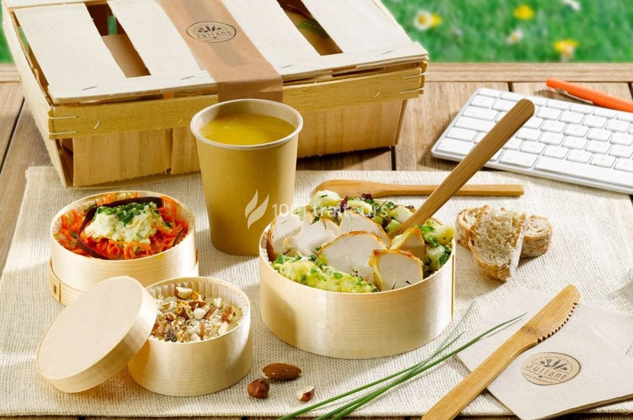 Repas équilibré présenté dans des contenants en bois, avec salade, poulet, dessert, jus et couverts écologiques.