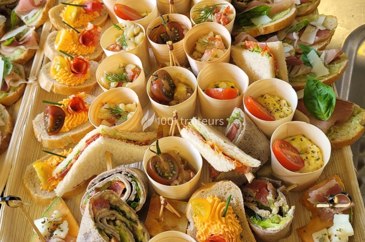 Plateau de bouchées variées comprenant sandwichs, roulés, verrines et garnitures colorées à base de légumes et herbes.