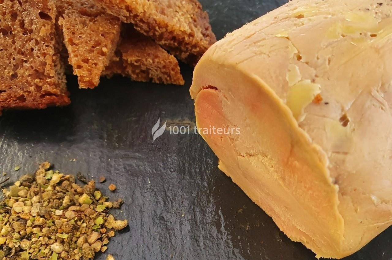 Bloc de foie gras avec des tranches de pain grillé et un mélange d'épices sur une assiette noire.