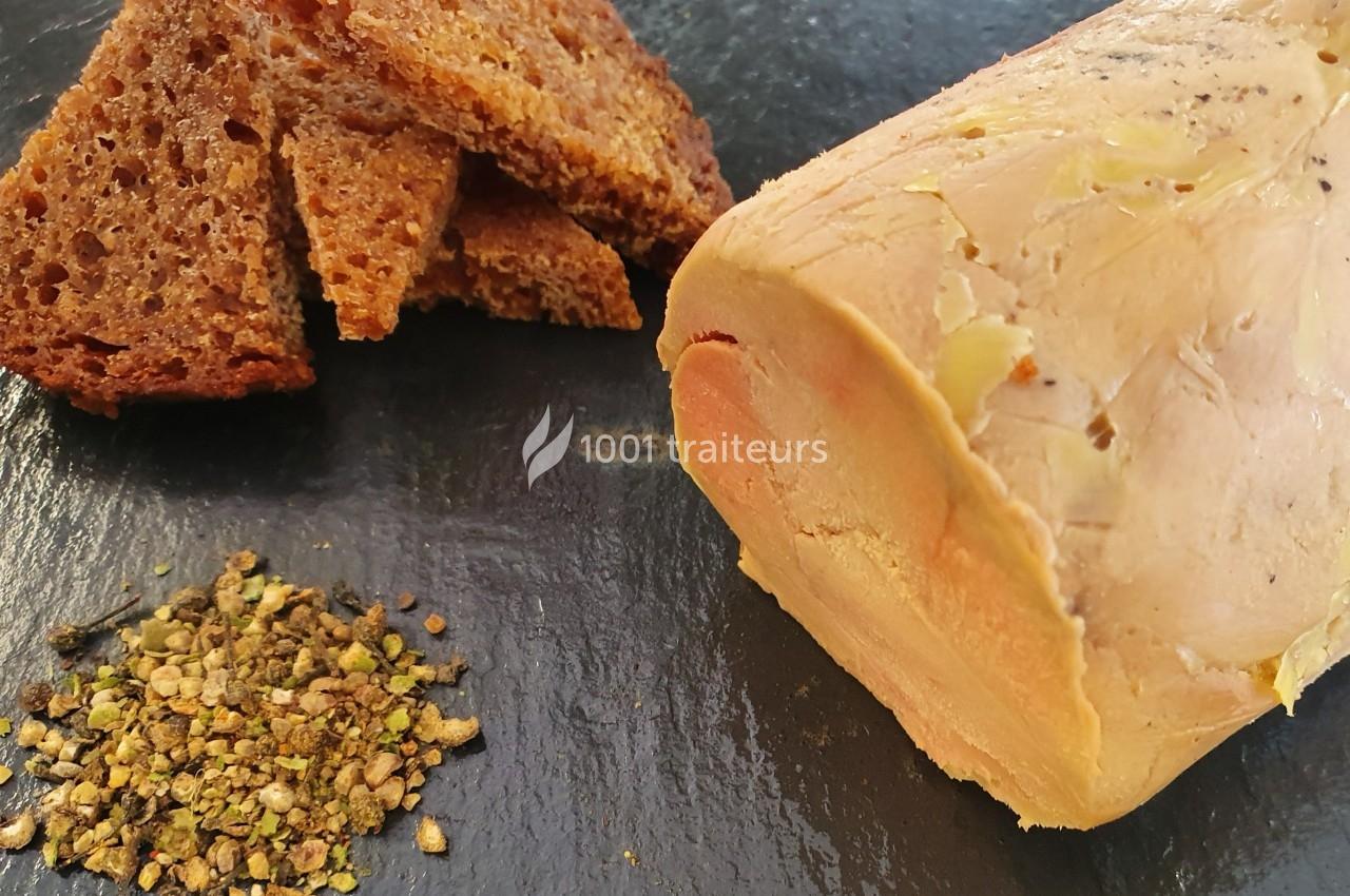 Bloc de foie gras accompagné de tranches de pain grillé et d'un mélange d'épices sur une ardoise noire.