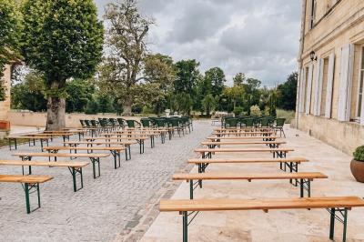 Une mariée en robe blanche et un marié en costume vert posent sur une voiture ancienne dans un cadre extérieur ensoleillé.