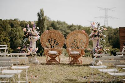 Une mariée en robe blanche et un marié en costume vert posent sur une voiture ancienne dans un cadre extérieur ensoleillé.