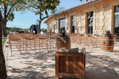 Une mariée en robe blanche et un marié en costume vert posent sur une voiture ancienne dans un cadre extérieur ensoleillé.