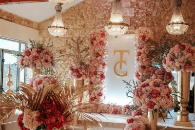 Une mariée en robe blanche et un marié en costume vert posent sur une voiture ancienne dans un cadre extérieur ensoleillé.