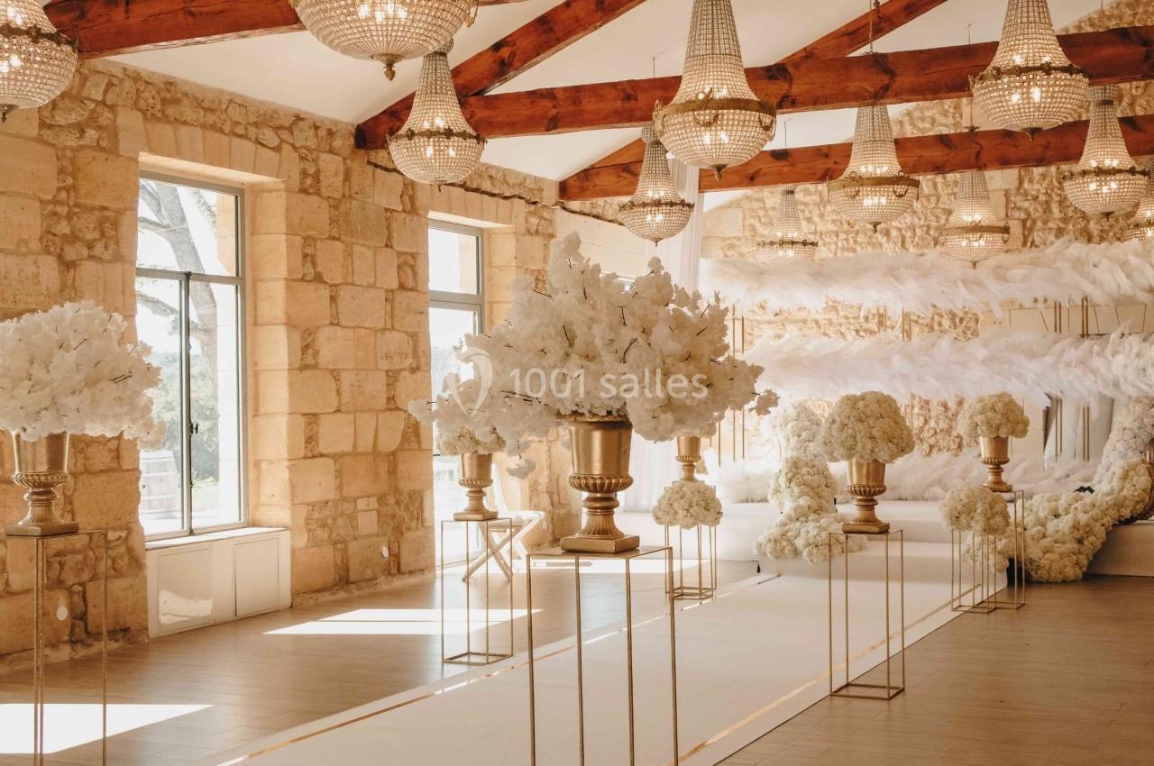 Salle de réception décorée avec des fleurs blanches, des lustres en cristal et des poutres en bois apparentes.