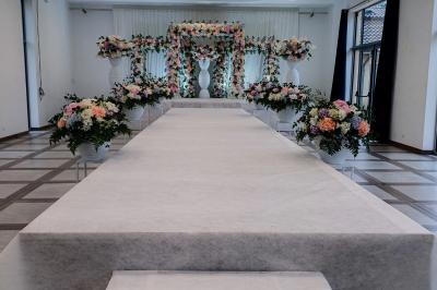 Une mariée en robe blanche et un marié en costume vert posent sur une voiture ancienne dans un cadre extérieur ensoleillé.