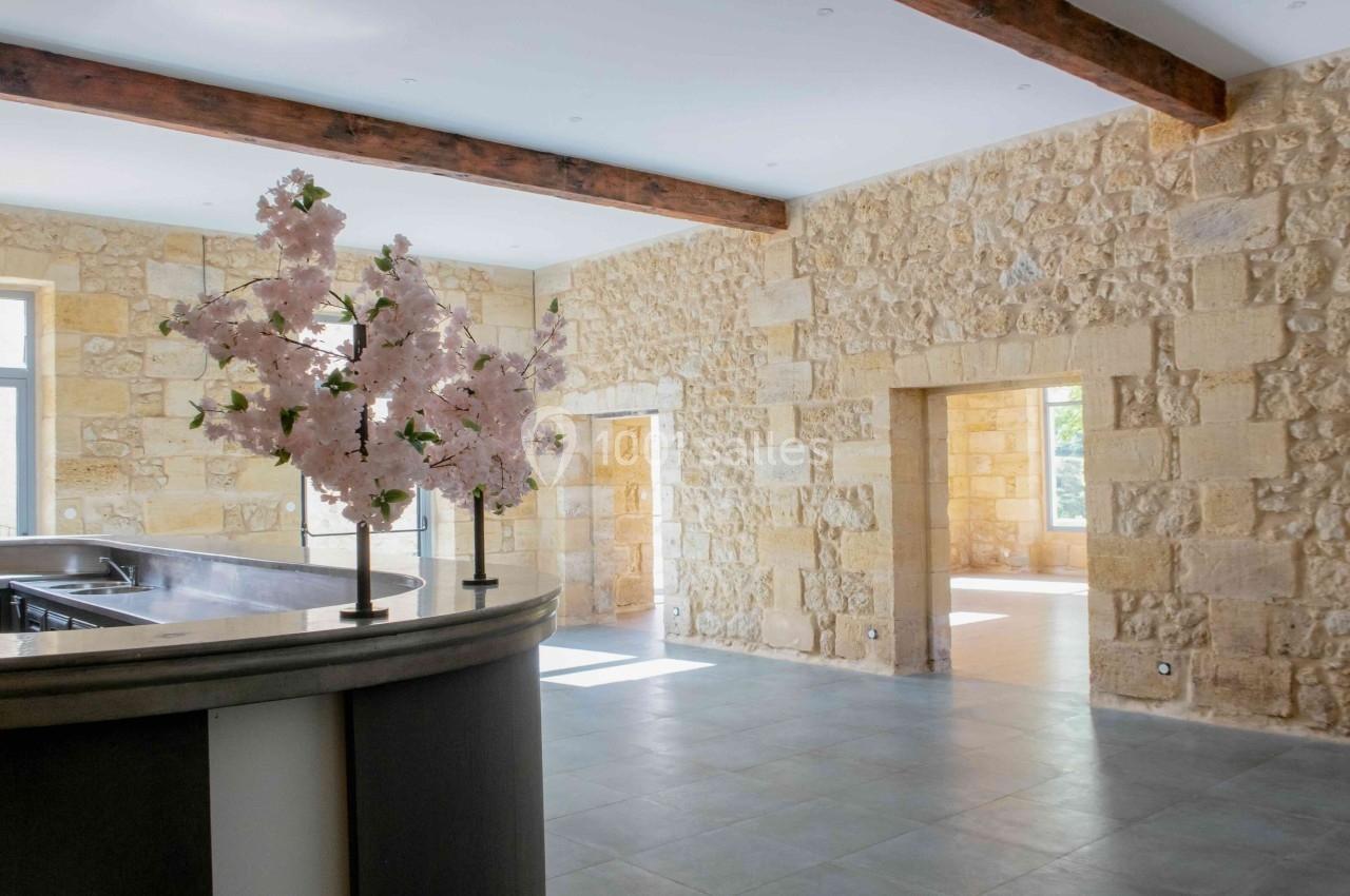 Salle lumineuse avec murs en pierre apparente, poutres en bois, comptoir moderne et décoration florale.