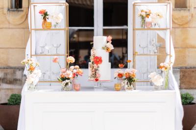 Une mariée en robe blanche et un marié en costume vert posent sur une voiture ancienne dans un cadre extérieur ensoleillé.