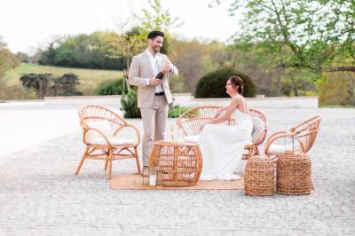Une mariée en robe blanche et un marié en costume vert posent sur une voiture ancienne dans un cadre extérieur ensoleillé.