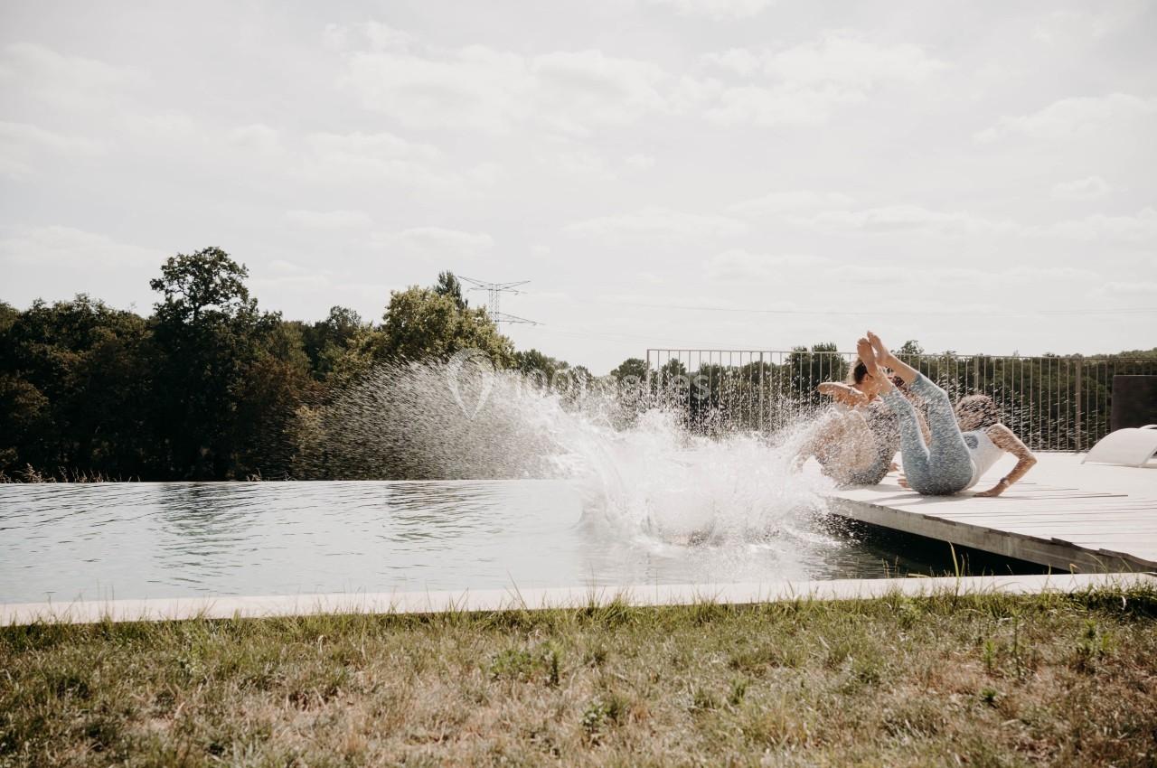 Deux personnes plongent dans une piscine depuis un ponton en bois, éclaboussant l'eau sous un ciel dégagé.