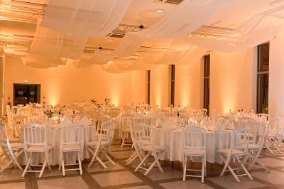 Une mariée en robe blanche et un marié en costume vert posent sur une voiture ancienne dans un cadre extérieur ensoleillé.