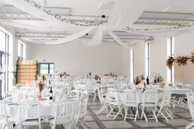 Une mariée en robe blanche et un marié en costume vert posent sur une voiture ancienne dans un cadre extérieur ensoleillé.