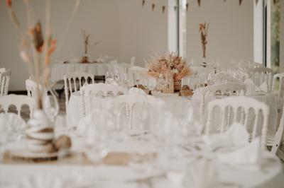 Une mariée en robe blanche et un marié en costume vert posent sur une voiture ancienne dans un cadre extérieur ensoleillé.