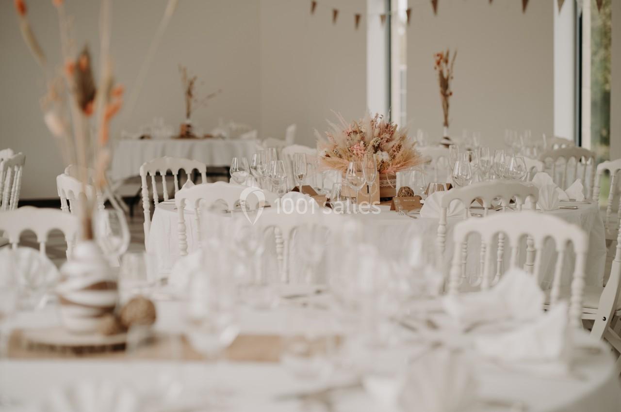 Salle de réception décorée avec des tables rondes, nappes blanches, chaises assorties et centres de table floraux.
