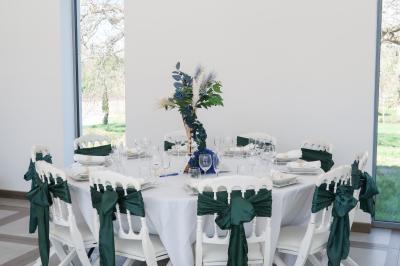 Une mariée en robe blanche et un marié en costume vert posent sur une voiture ancienne dans un cadre extérieur ensoleillé.