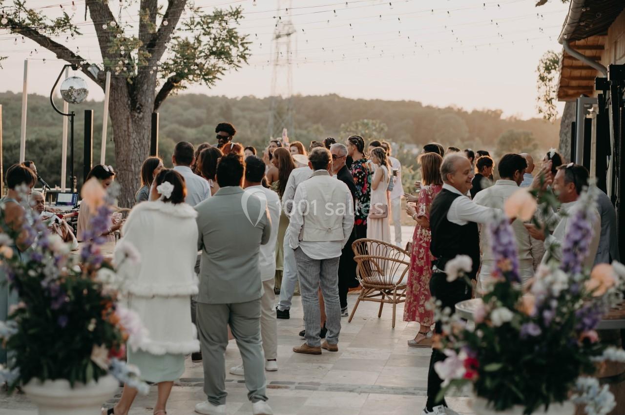 Groupe de personnes rassemblées en extérieur lors d'un événement, entourées de fleurs et éclairées par des guirlandes…
