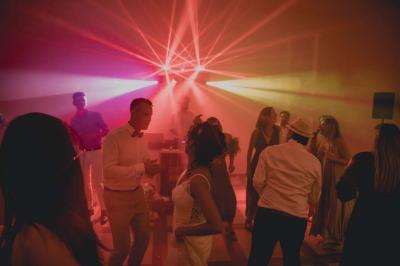 Une mariée en robe blanche et un marié en costume vert posent sur une voiture ancienne dans un cadre extérieur ensoleillé.
