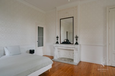 Salon lumineux avec murs en pierre apparente, canapé gris, table basse et grandes fenêtres laissant entrer la lumière.