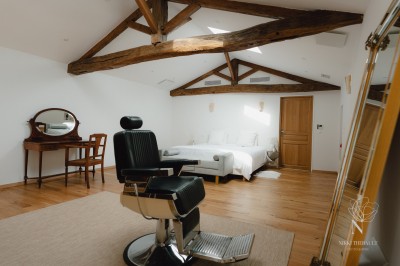 Salon lumineux avec murs en pierre apparente, canapé gris, table basse et grandes fenêtres laissant entrer la lumière.