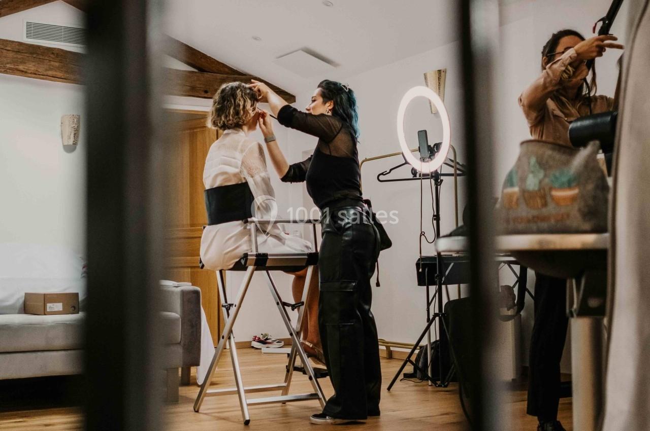 Une femme assise se fait coiffer et maquiller dans un salon avec des équipements professionnels.