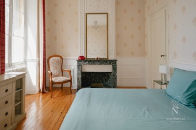 Salon lumineux avec murs en pierre apparente, canapé gris, table basse et grandes fenêtres laissant entrer la lumière.