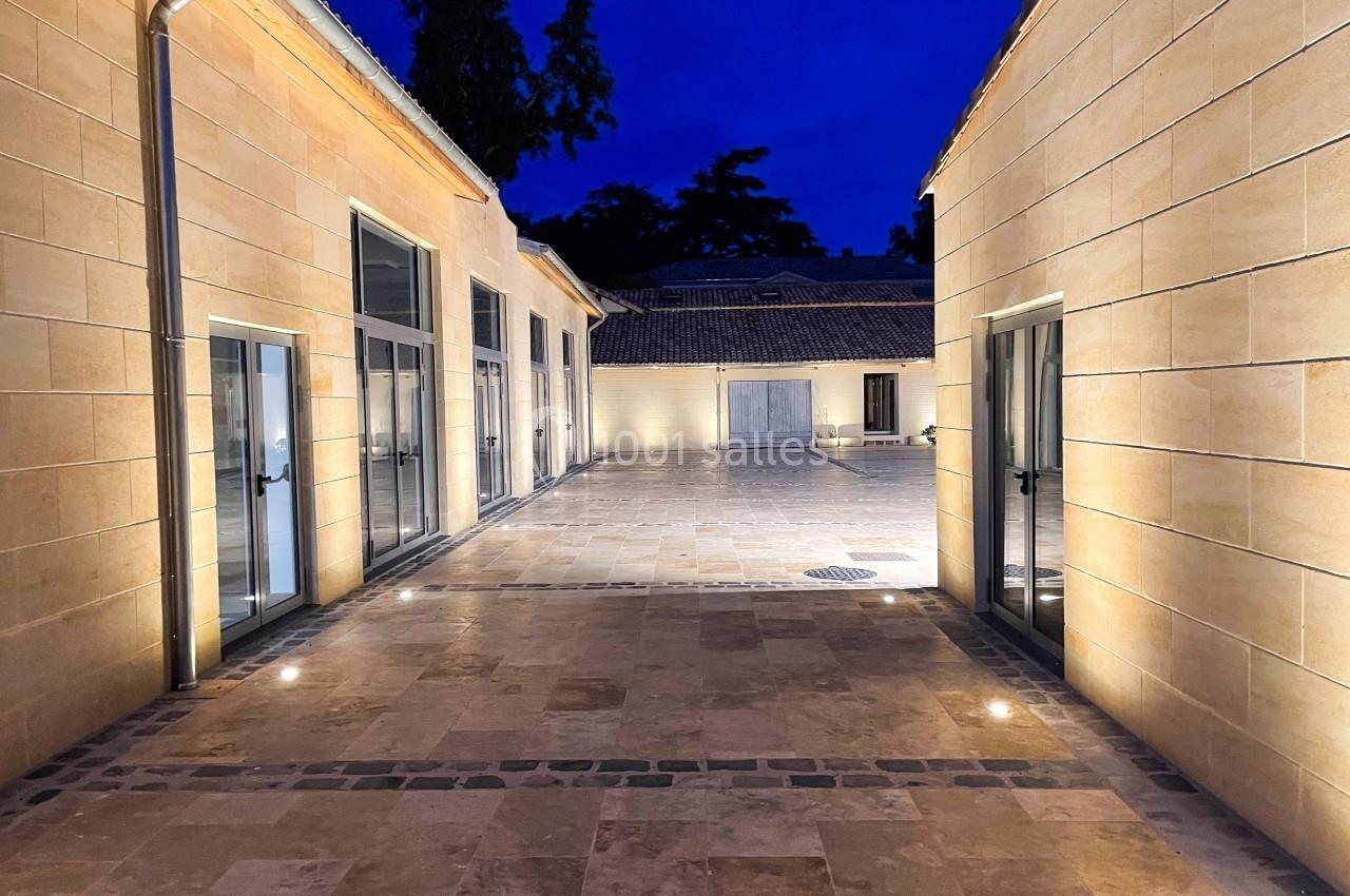 Cour pavée éclairée par des lumières au sol, entourée de bâtiments aux façades en pierre, sous un ciel nocturne.