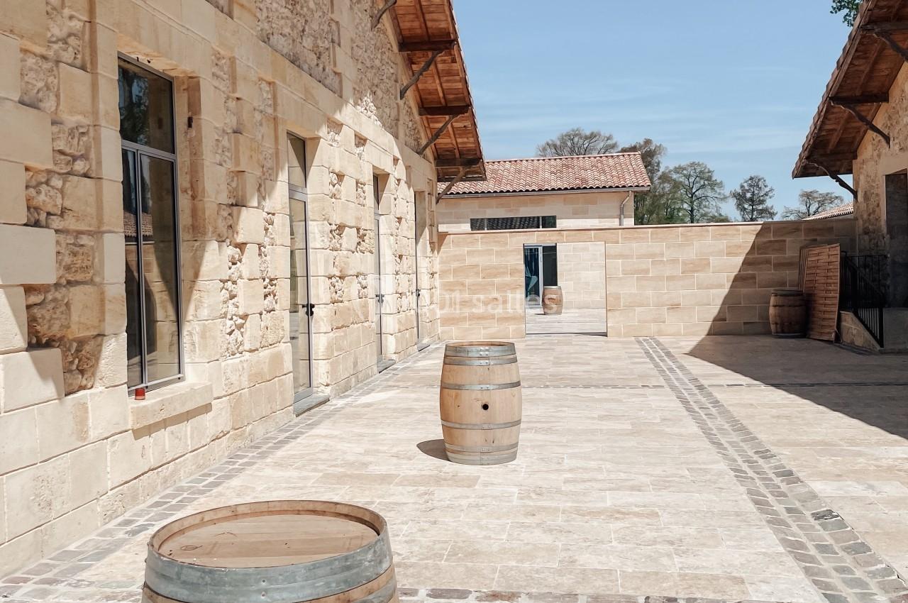 Cour pavée ensoleillée avec des tonneaux en bois devant des bâtiments en pierre aux toits en tuiles.