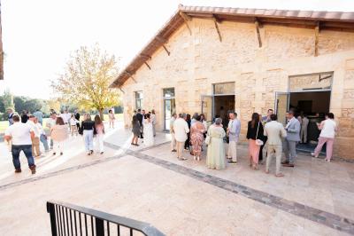 Une mariée en robe blanche et un marié en costume vert posent sur une voiture ancienne dans un cadre extérieur ensoleillé.