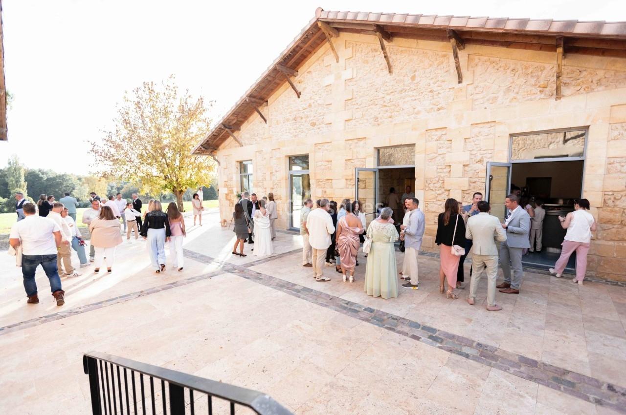 Groupe de personnes rassemblées devant un bâtiment en pierre, sous un ciel clair, lors d'un événement en extérieur.