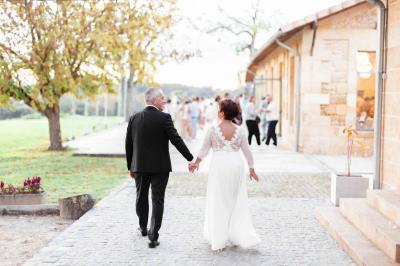 Une mariée en robe blanche et un marié en costume vert posent sur une voiture ancienne dans un cadre extérieur ensoleillé.