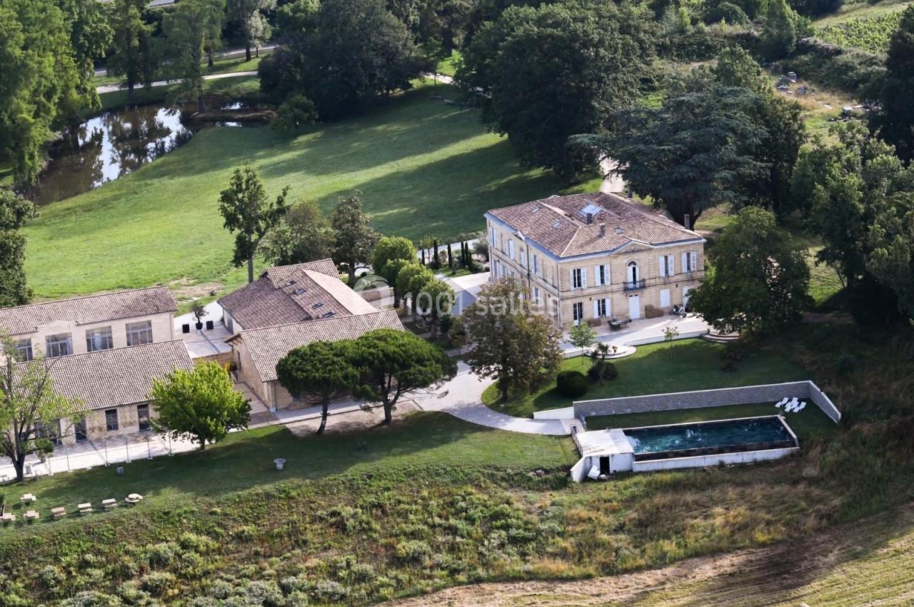 Vue aérienne d'une propriété avec une maison en pierre, piscine, bâtiments annexes et espaces verts environnants.