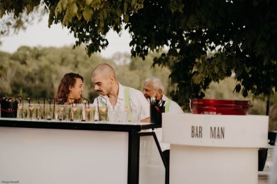 Miniature Bar extérieur - ©Hugo Herault Façade d'un bâtiment en pierre avec grandes baies vitrées illuminées par des lumières roses à la tombée de la nuit.