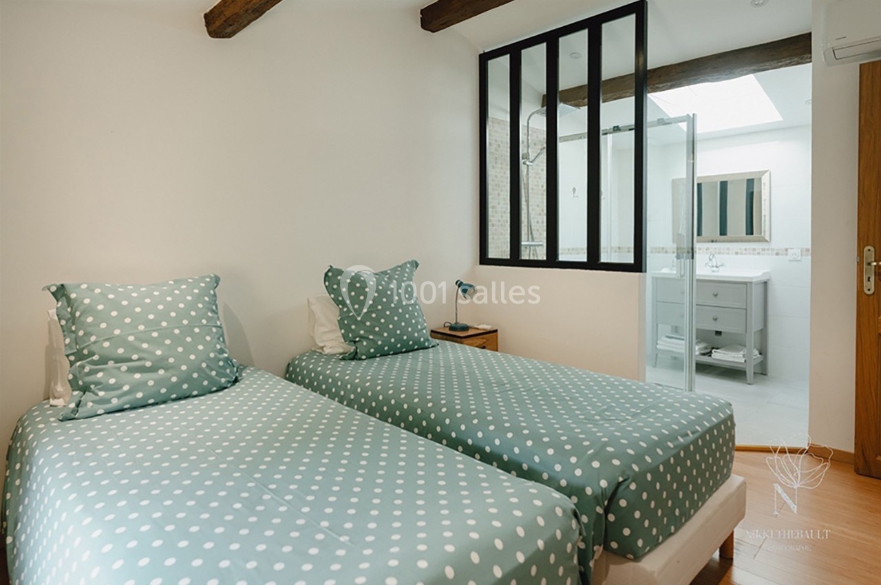 Deux lits simples avec housses à pois verts dans une chambre lumineuse, vue sur une salle de bain attenante.