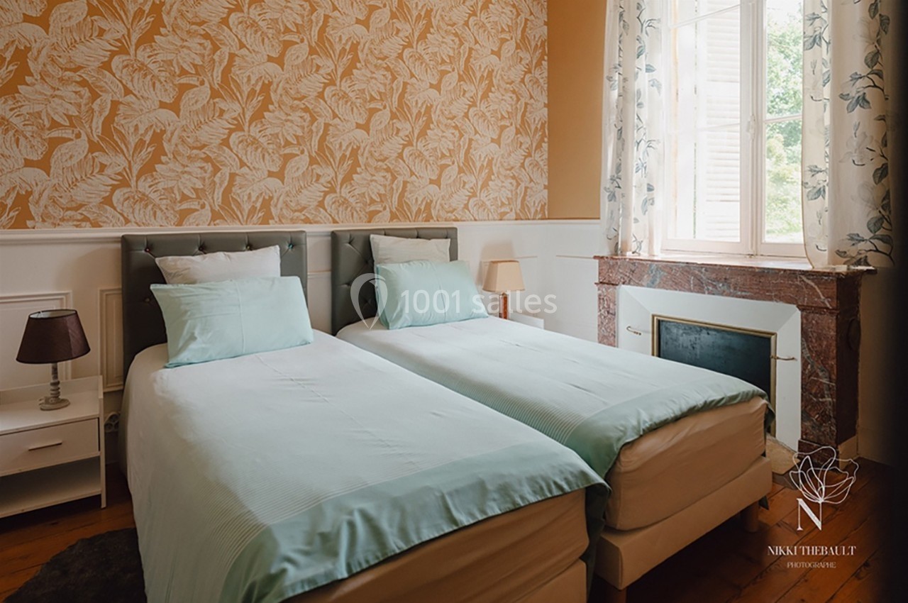 Deux lits simples avec draps turquoise dans une chambre lumineuse, décorée de papier peint à motifs et d'une cheminée en…