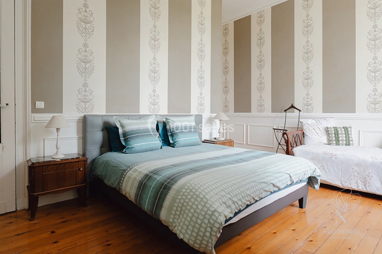 Chambre lumineuse avec lit double, linge de lit vert, murs à motifs et sol en parquet.