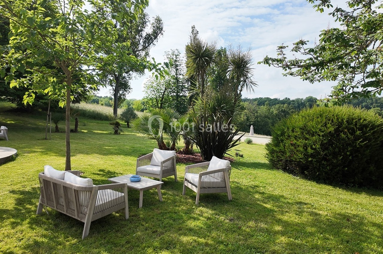 Mobilier de jardin en bois avec coussins blancs disposé sur une pelouse entourée d'arbres et de végétation.