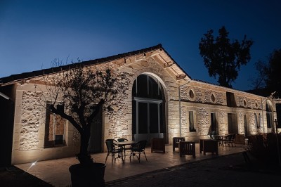 Miniature Logements extérieurs de nuit Façade d'un bâtiment en pierre avec grandes baies vitrées illuminées par des lumières roses à la tombée de la nuit.