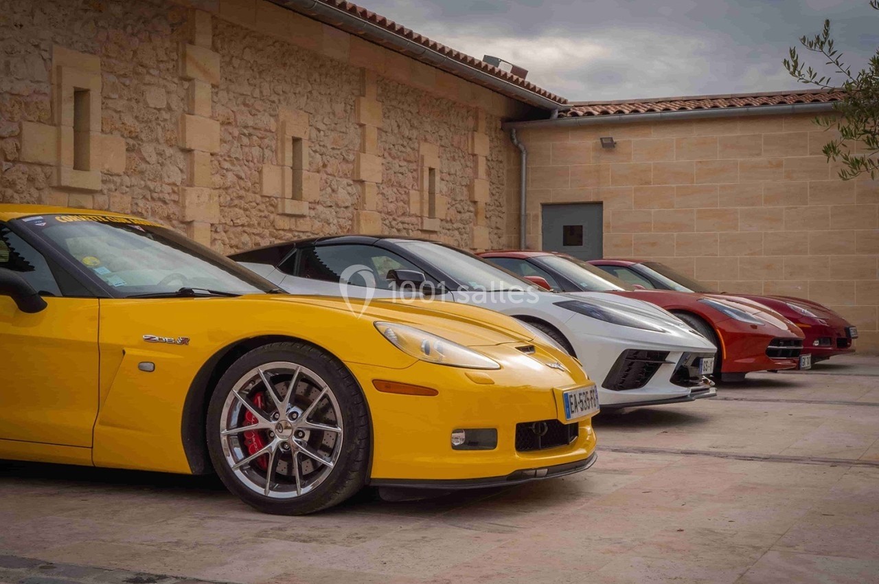 Quatre voitures de sport alignées devant un bâtiment en pierre sous un ciel nuageux.
