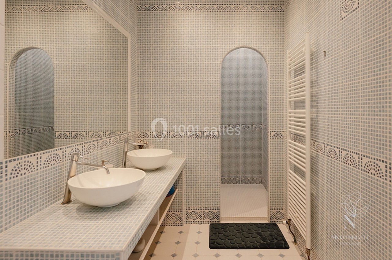 Salle de bain avec murs en mosaïque bleue, double vasque blanche, miroir large et douche à l'italienne.