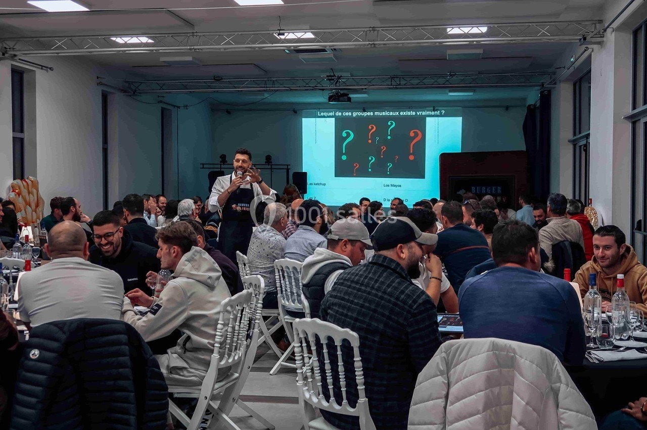 Un animateur pose une question à un public assis lors d'un événement dans une salle éclairée.