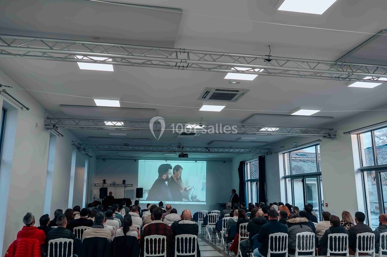 Salle de conférence avec un public assis regardant une projection sur grand écran.