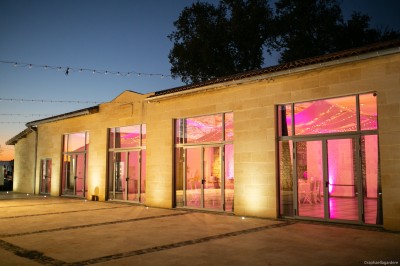 Miniature Salle de séminaire de nuit ©raphaellagardere Façade d'un bâtiment en pierre avec grandes baies vitrées illuminées par des lumières roses à la tombée de la nuit.