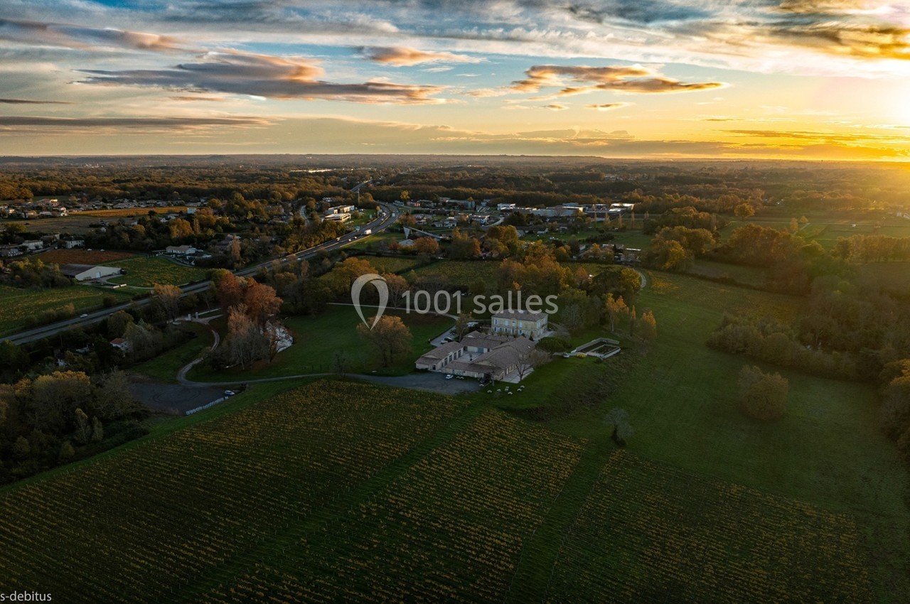 Vue aérienne d'un domaine entouré de vignes et de paysages ruraux au coucher du soleil.