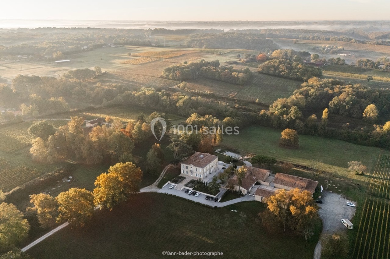 Vue aérienne d'un domaine entouré de champs, de vignes et d'arbres, baigné par une lumière douce au lever du soleil.