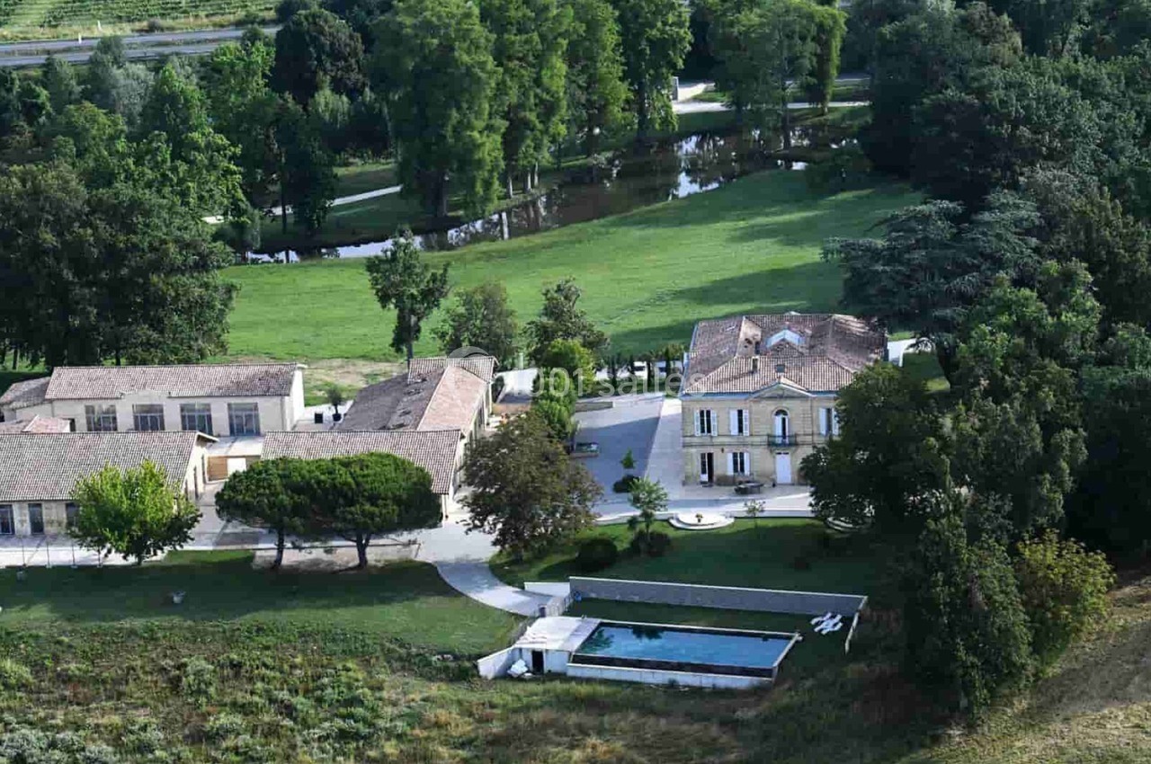 Vue aérienne d'une propriété avec une maison en pierre, des bâtiments annexes, une piscine et un espace vert arboré.